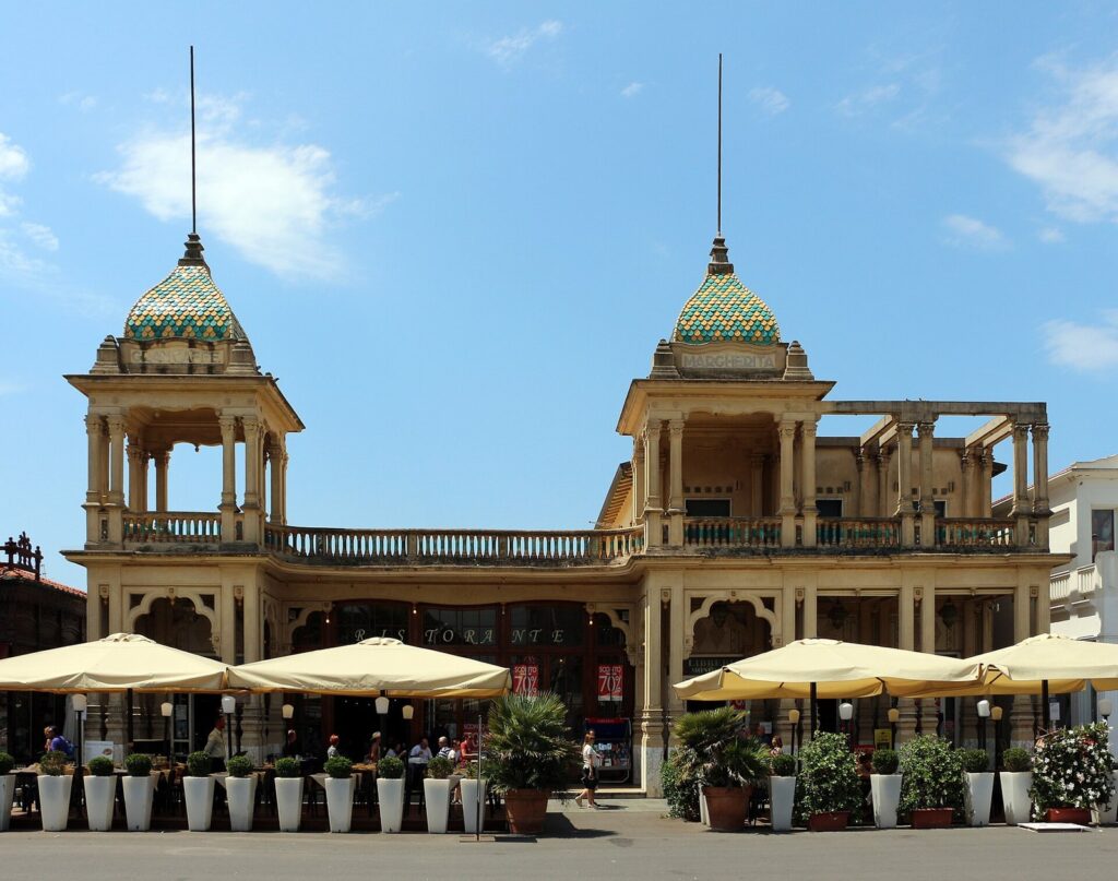 La facciata liberty del Gran Caffè Margherita sulla Passeggiata di Viareggio, con le due torrette rivestite di maiolica e i tavolini sotto gli ombrelloni